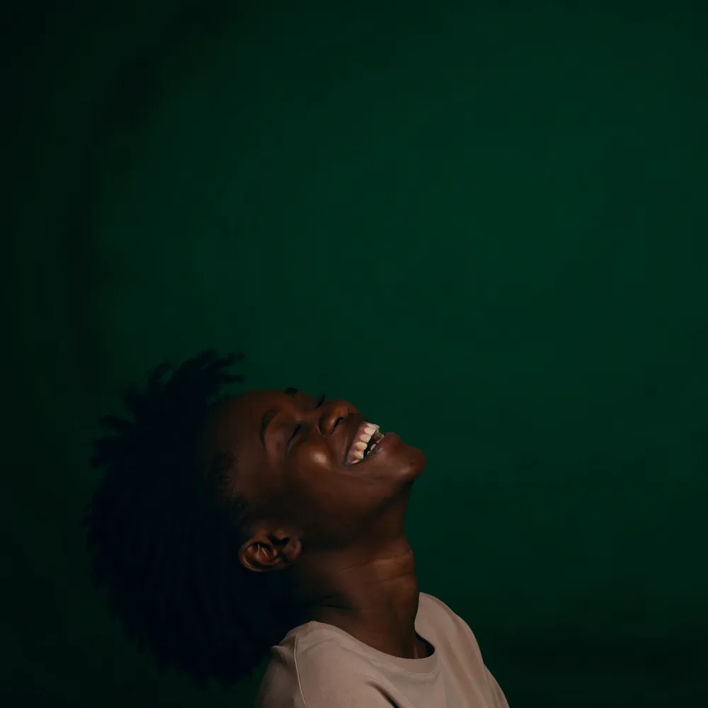 A woman laughing against a deep green background