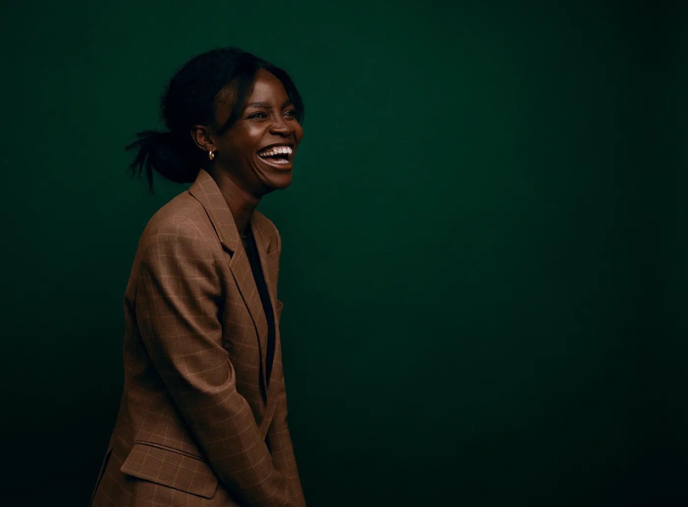 A woman laughing, photographed against a deep forest green background