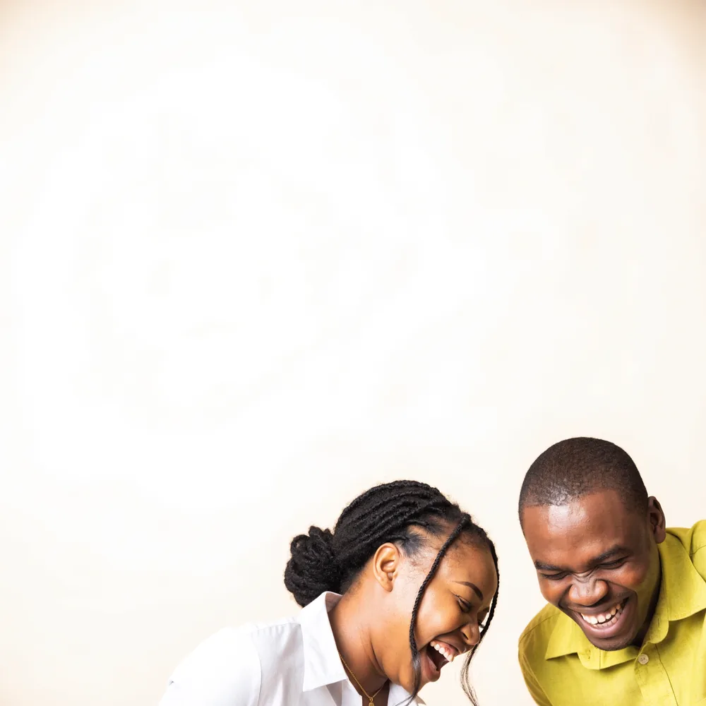 Two colleagues laughing together against a cream background