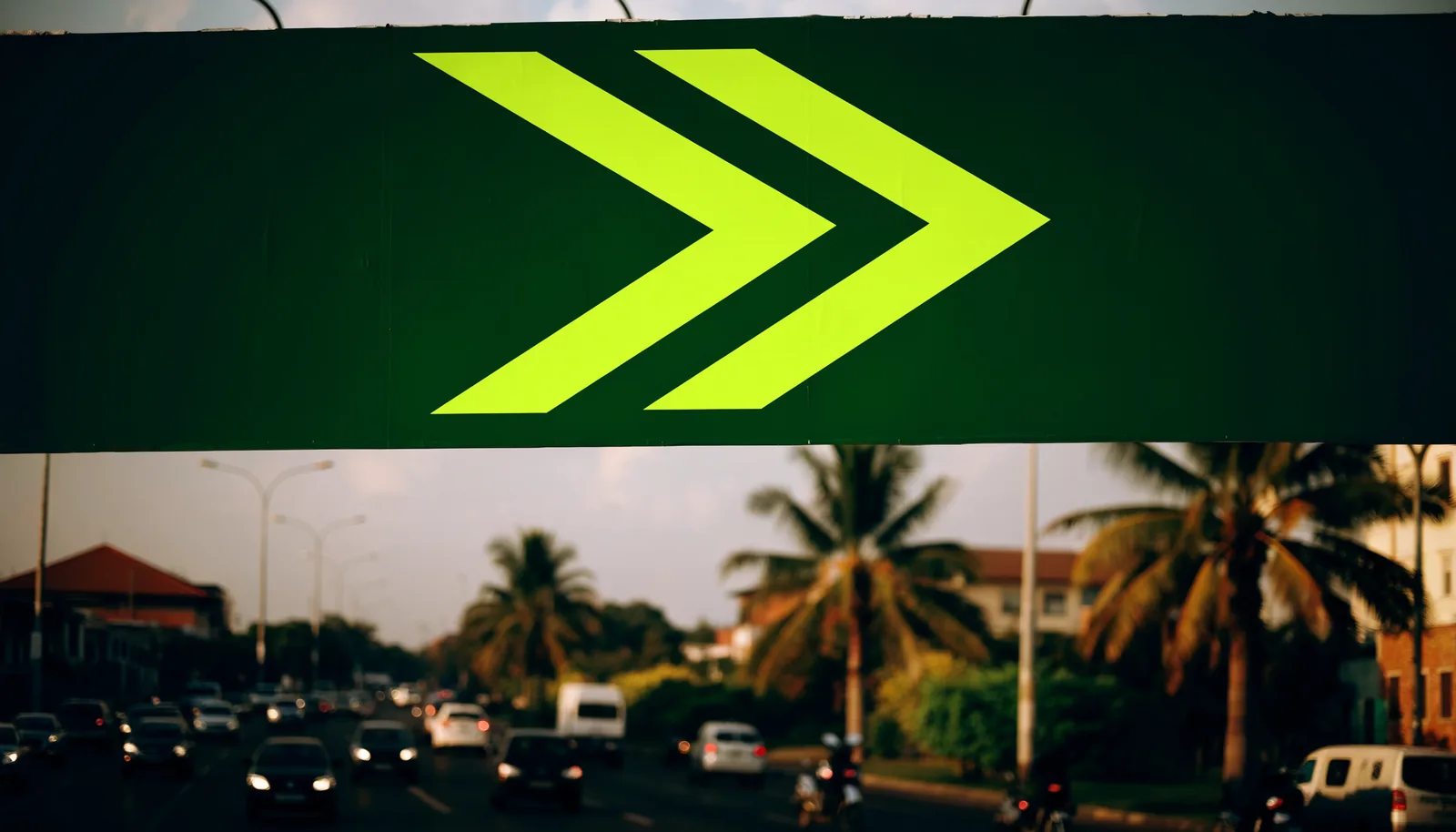 A deep green billboard carrying the volt chevron mark above a busy Accra road at golden hour