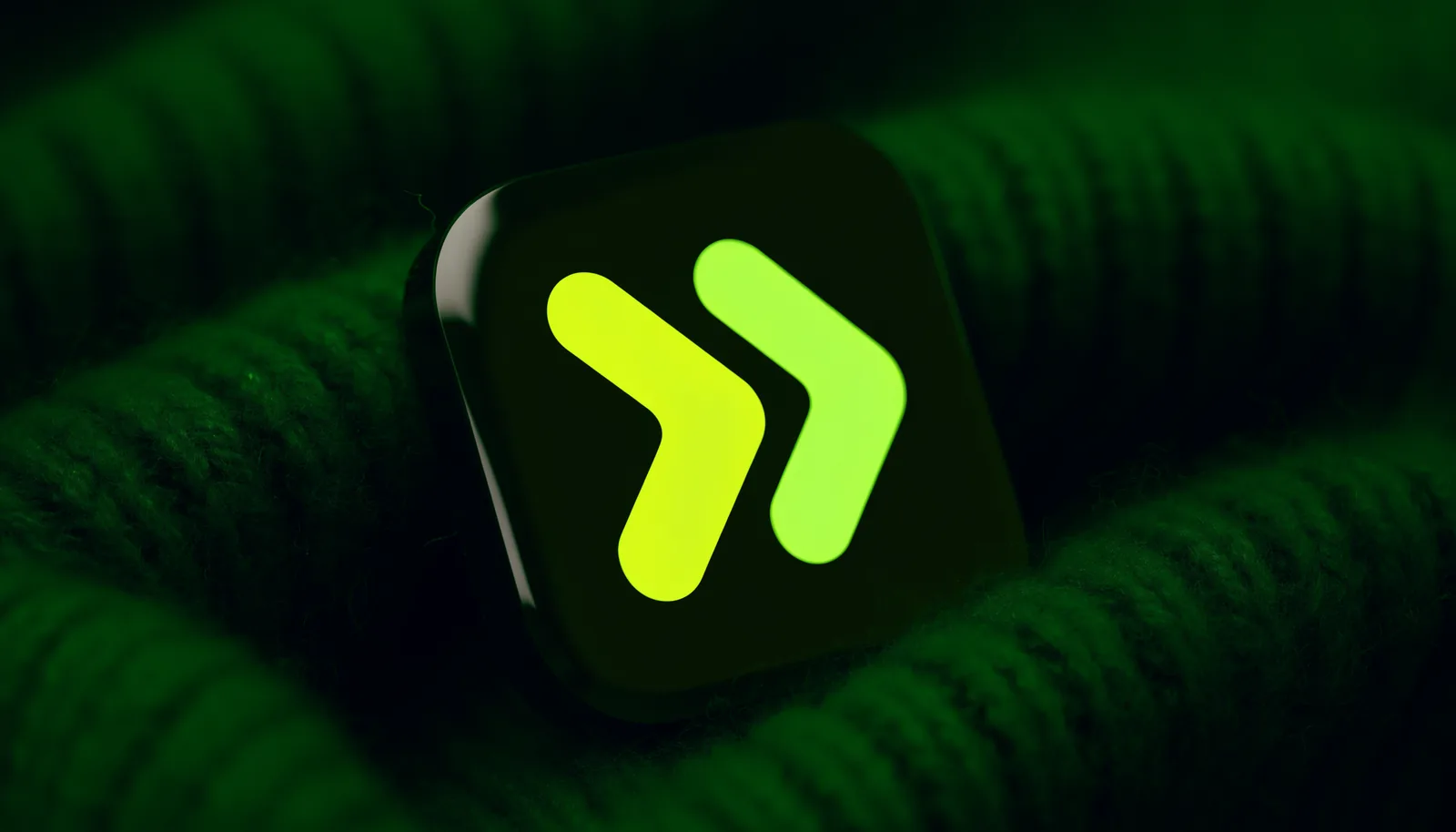 The AmplifyPay app icon as a glossy object resting on deep green knitted wool