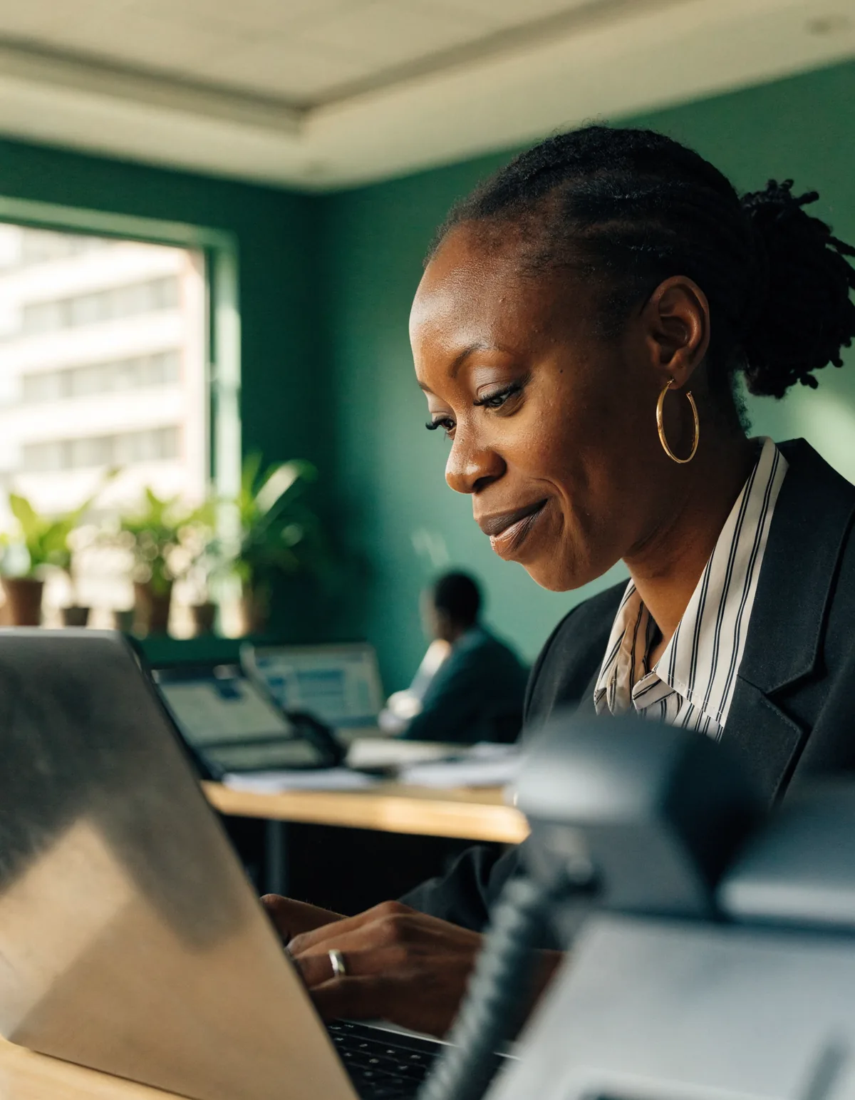 A payroll officer in an Accra office working at her laptop in window light