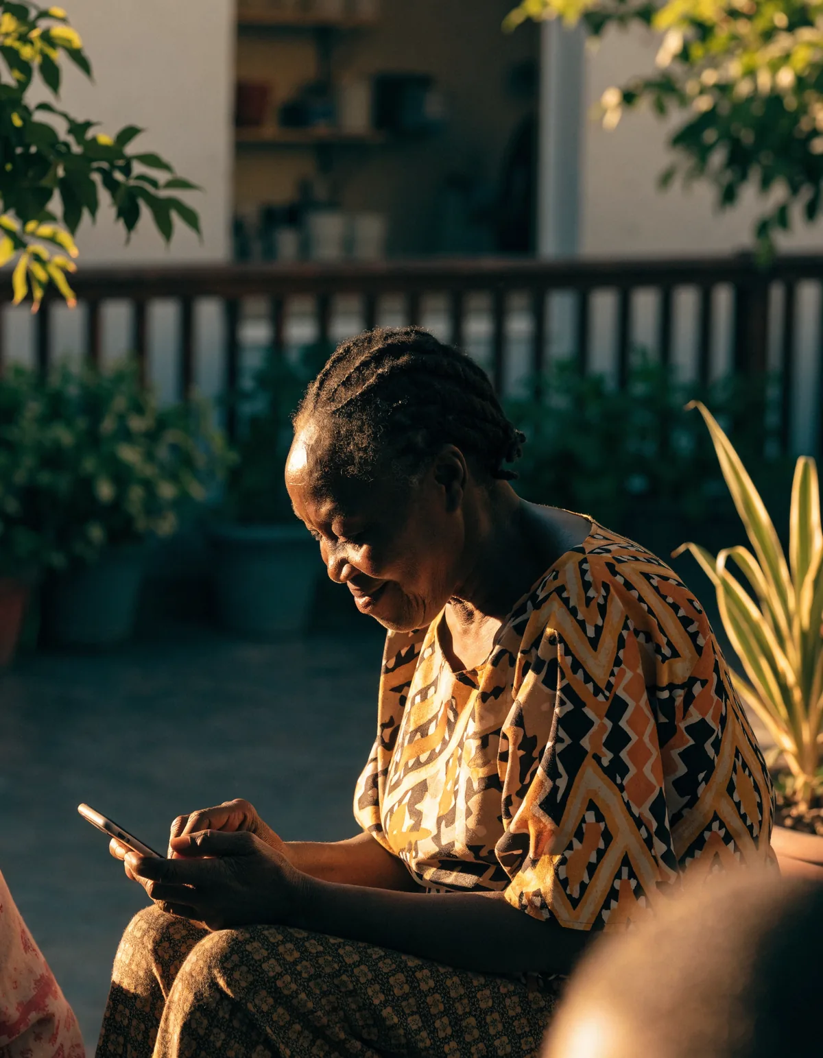A woman on her veranda in Accra in late afternoon light, looking at her phone
